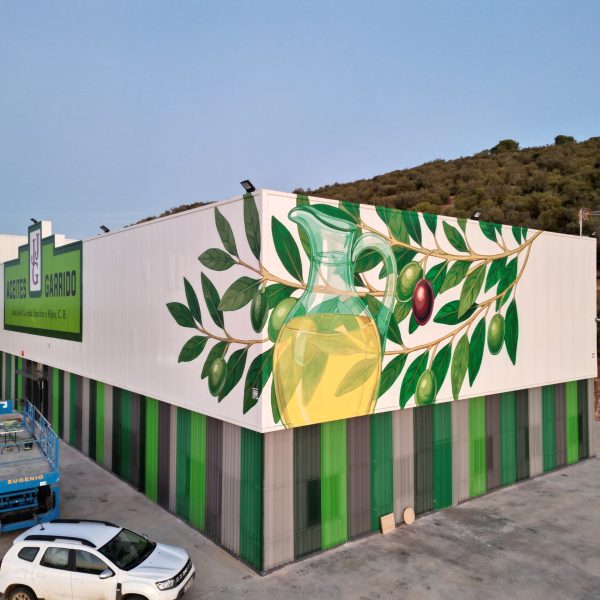 Mural corporativo pintado en una pared exterior para Aceites Garrido que muestra un diseño artístico de aceitunas y aceite, integrando la identidad visual de la marca en la fachada.